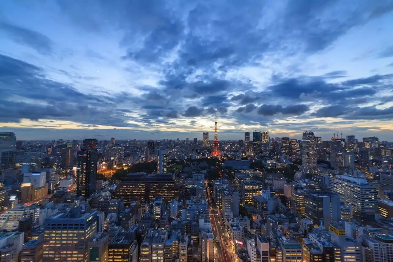 Global Markets Never Sleep - A wide cityscape shot at dusk showing illuminated office towers against a deep blue sky. The image should capture the 'blue hour' when building lights are on but there's still color in the sky. Any major financial district (NYC, London, Hong Kong) works.